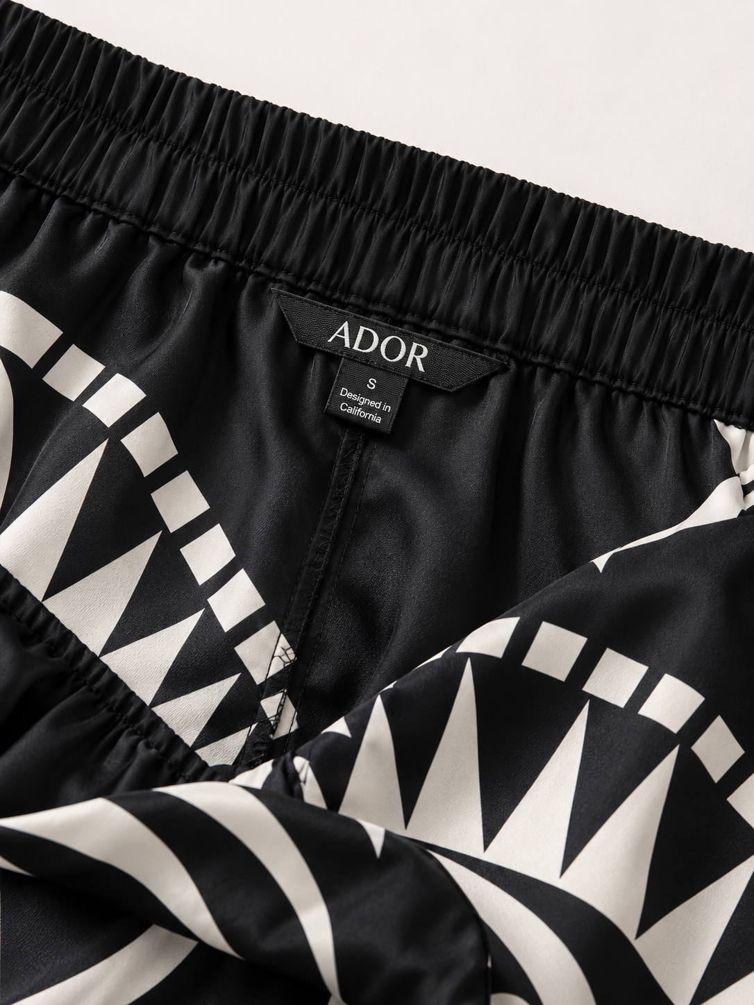 ADOR brand label detail on Noir Geometry Silky Satin Wide Leg Pants